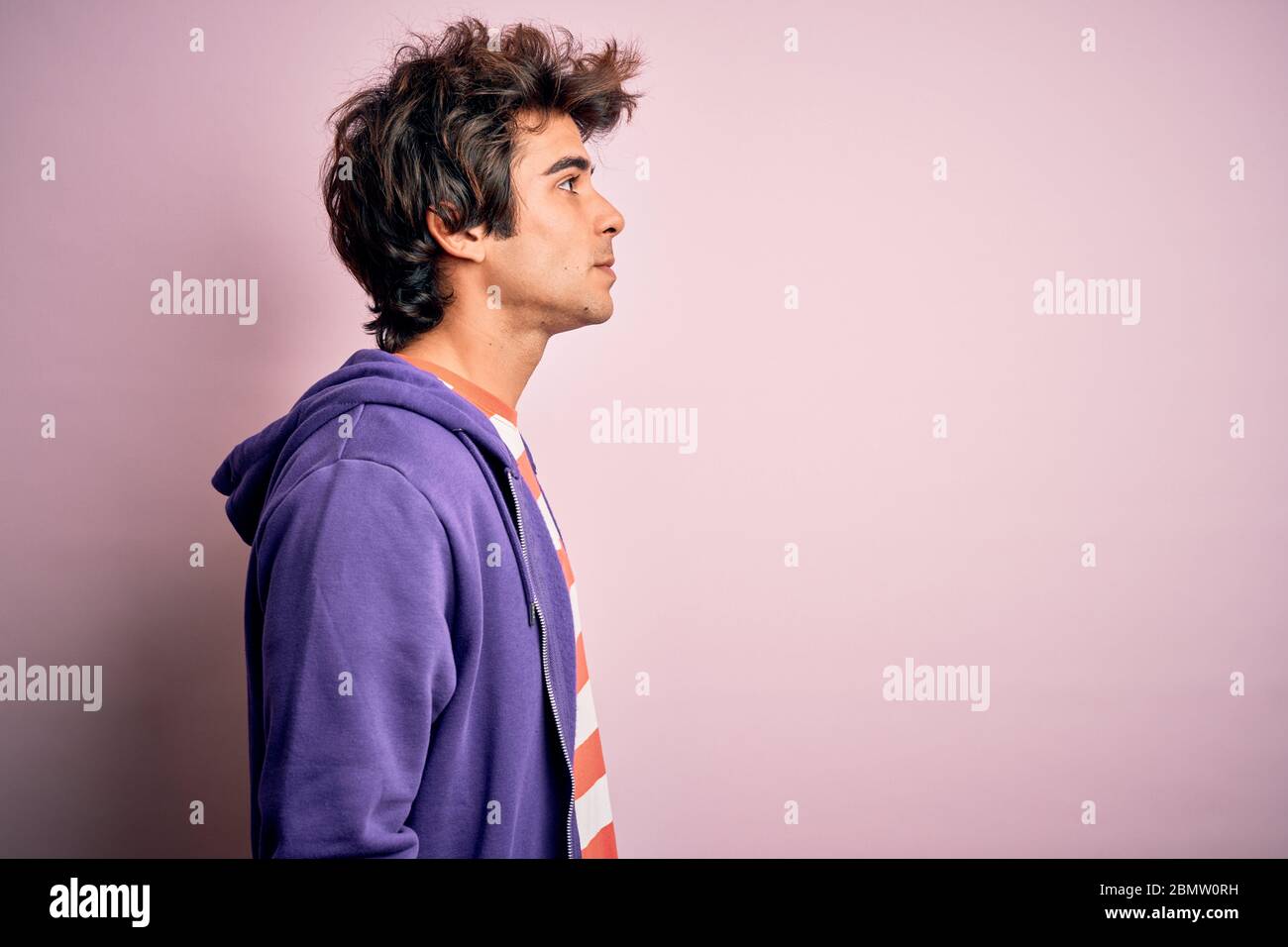 Jeune homme portant un t-shirt rayé et un sweat-shirt violet sur un arrière-plan rose isolé regardant sur le côté, relax profil pose avec visage naturel avec confid Banque D'Images