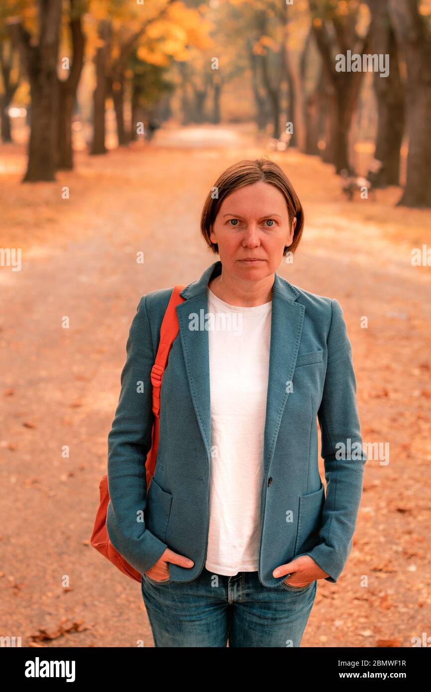 Portrait of businesswoman in autumn park, debout sur sentier entre les arbres avec un feuillage dynamique Banque D'Images