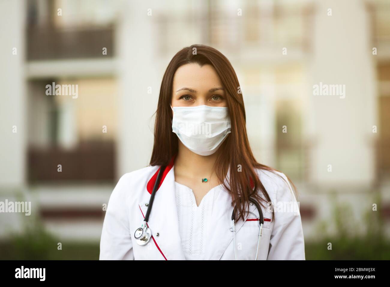 Concept de conférence ou de séminaire en ligne : jeune femme médecin en masque chirurgical et oreillettes en extérieur Banque D'Images