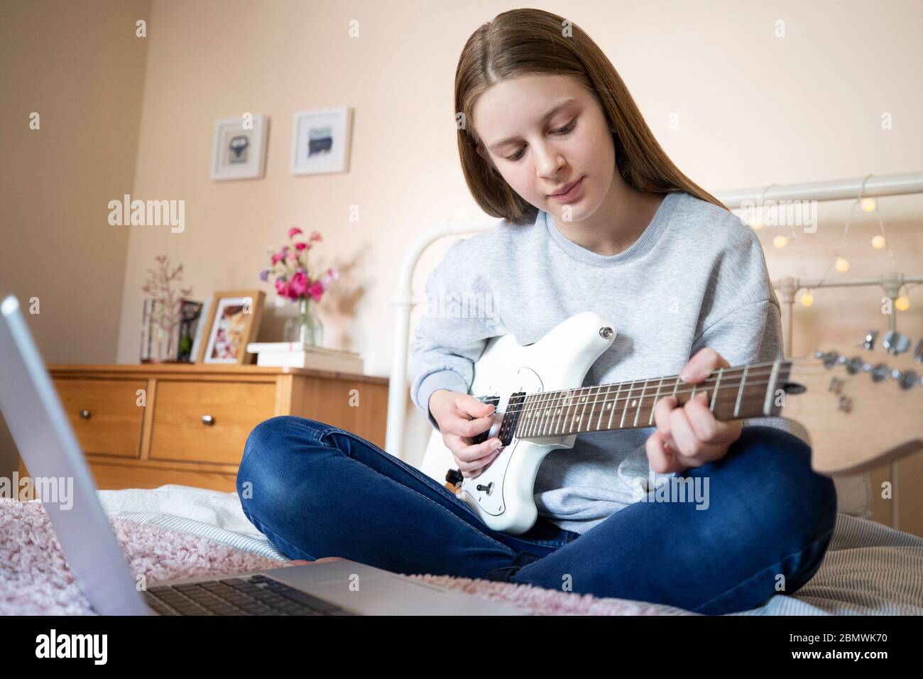 Adolescente assise sur le lit apprendre à jouer de la guitare électrique  avec leçon en ligne sur ordinateur portable Photo Stock - Alamy