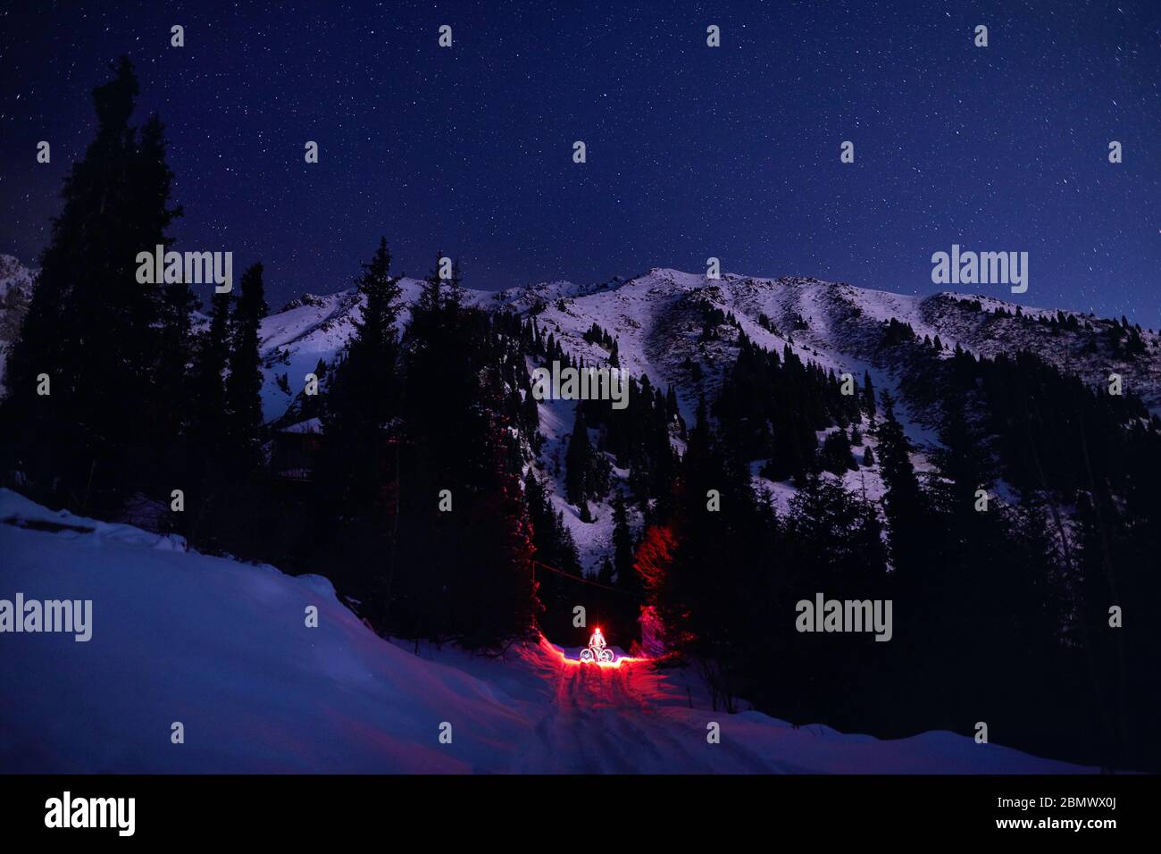 L'homme en rouge veste avec location et lumière rougeoyante à l'hiver la forêt enneigée dans les montagnes sous le ciel de nuit avec des étoiles Banque D'Images