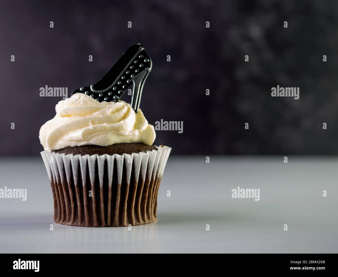 Cupcake au chocolat avec glaçage blanc et haut tourbé et un talon haut à pois noir et argent, posé sur le dessus avec un comptoir blanc et du marbre noir Banque D'Images