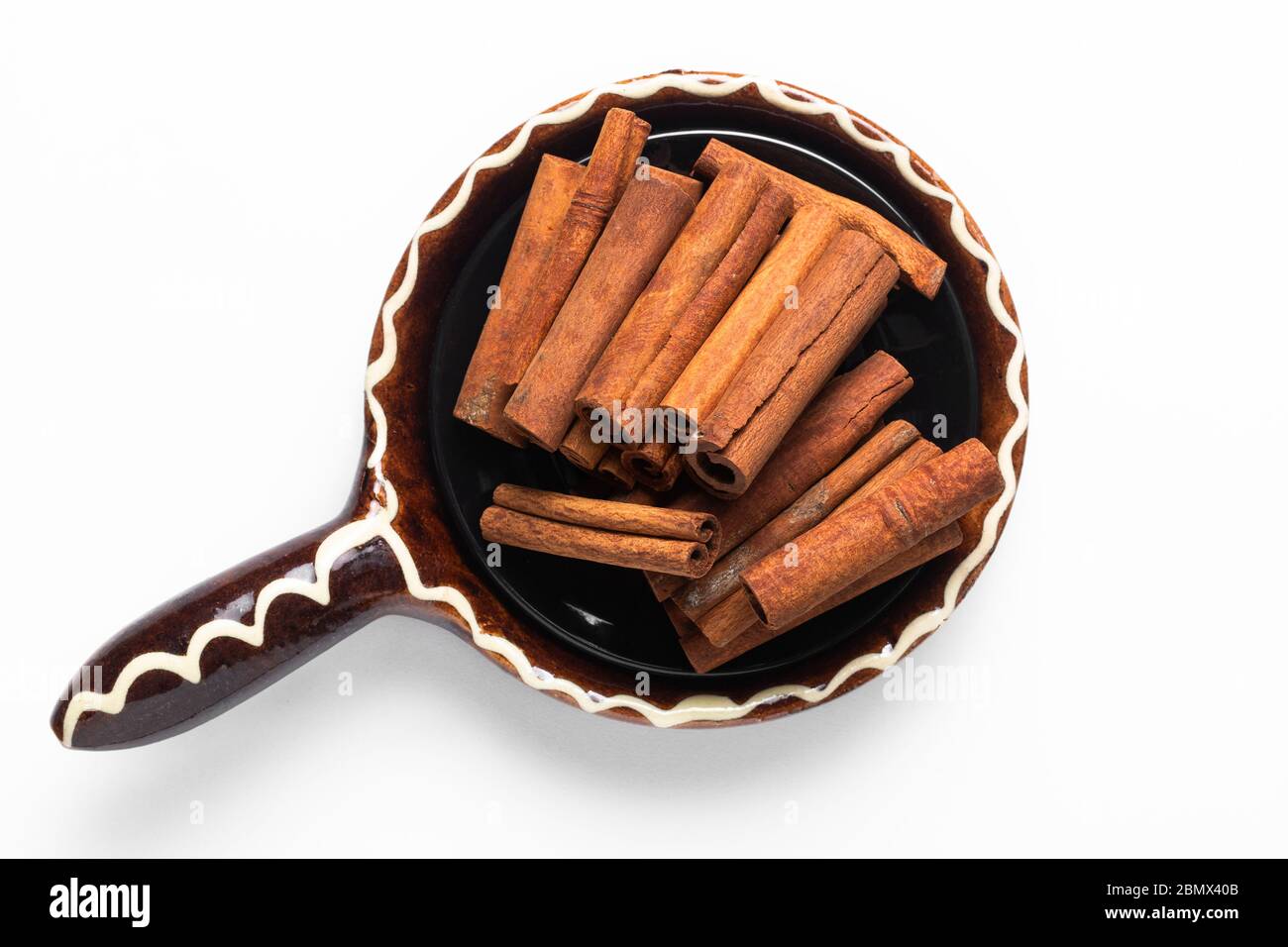 Ingrédient alimentaire sain bâtons de cannelle biologique dans un bol en céramique brun à poignée sur fond blanc Banque D'Images