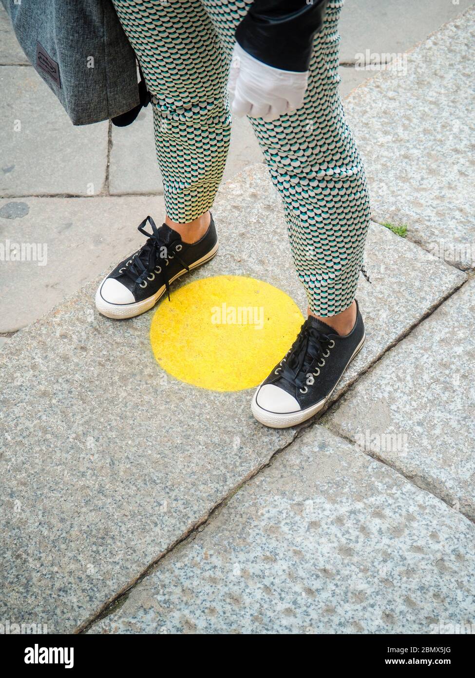 Les jambes et les pieds d'une personne attendant dans la ligne et debout à l'intérieur des cercles jaunes avec des mesures de distanciation sociale après l'éclosion du coronavirus. Banque D'Images