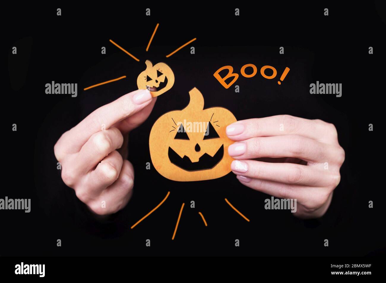 Les mains des femmes portant des petits citrouilles drôles sur fond noir. Carte d'Halloween avec inscription Boo. Banque D'Images