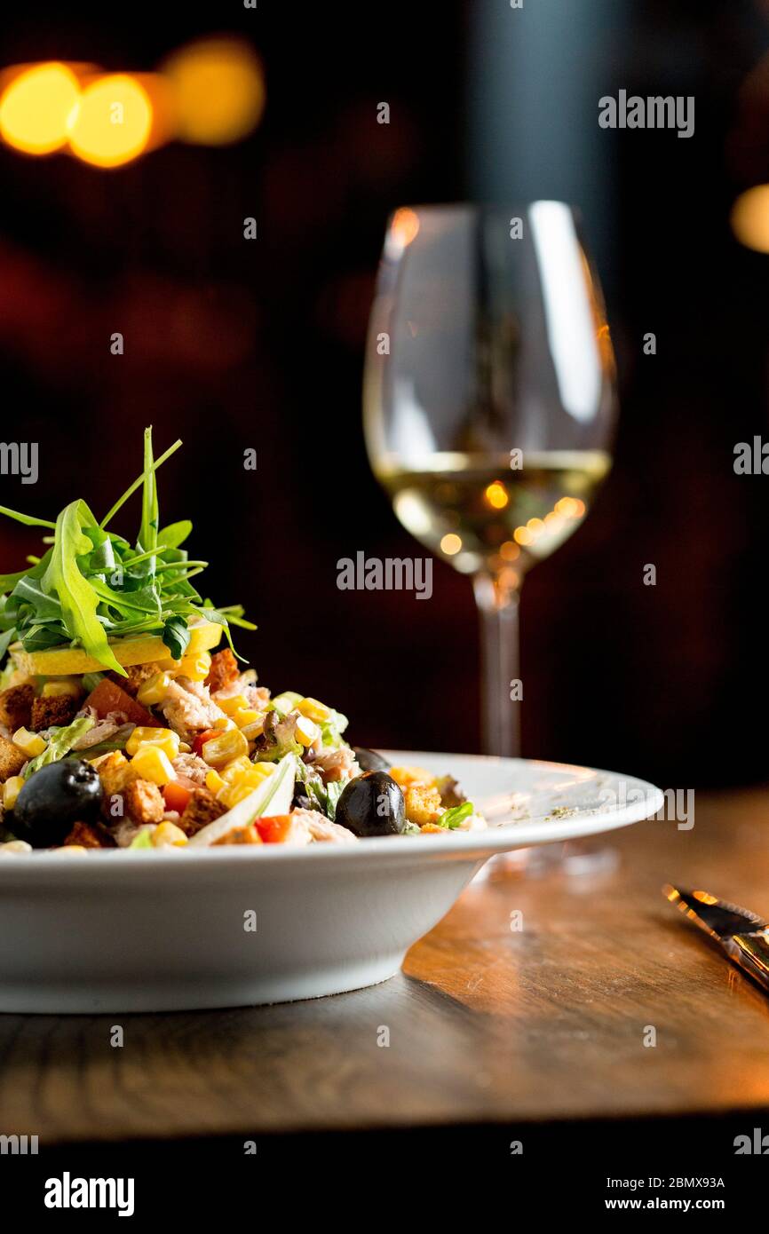 Salade de tun aux olives, maïs et roquette sur la table avec un verre de vin blanc Banque D'Images