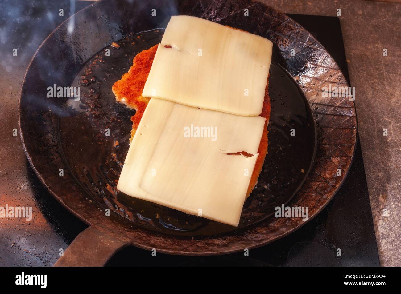 Schnitzel recouvert de fromage dans une poêle forgée à la main pendant la cuisson Banque D'Images
