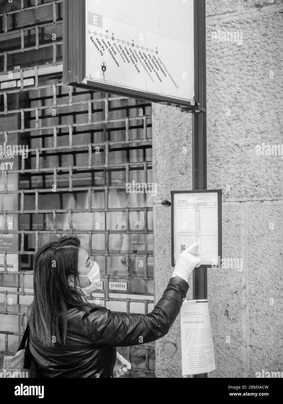 femme caucasique adulte portant un masque médical et des gants de protection stériles, lisant la liste des arrêts de bus et des informations en attendant le bus à venir Banque D'Images