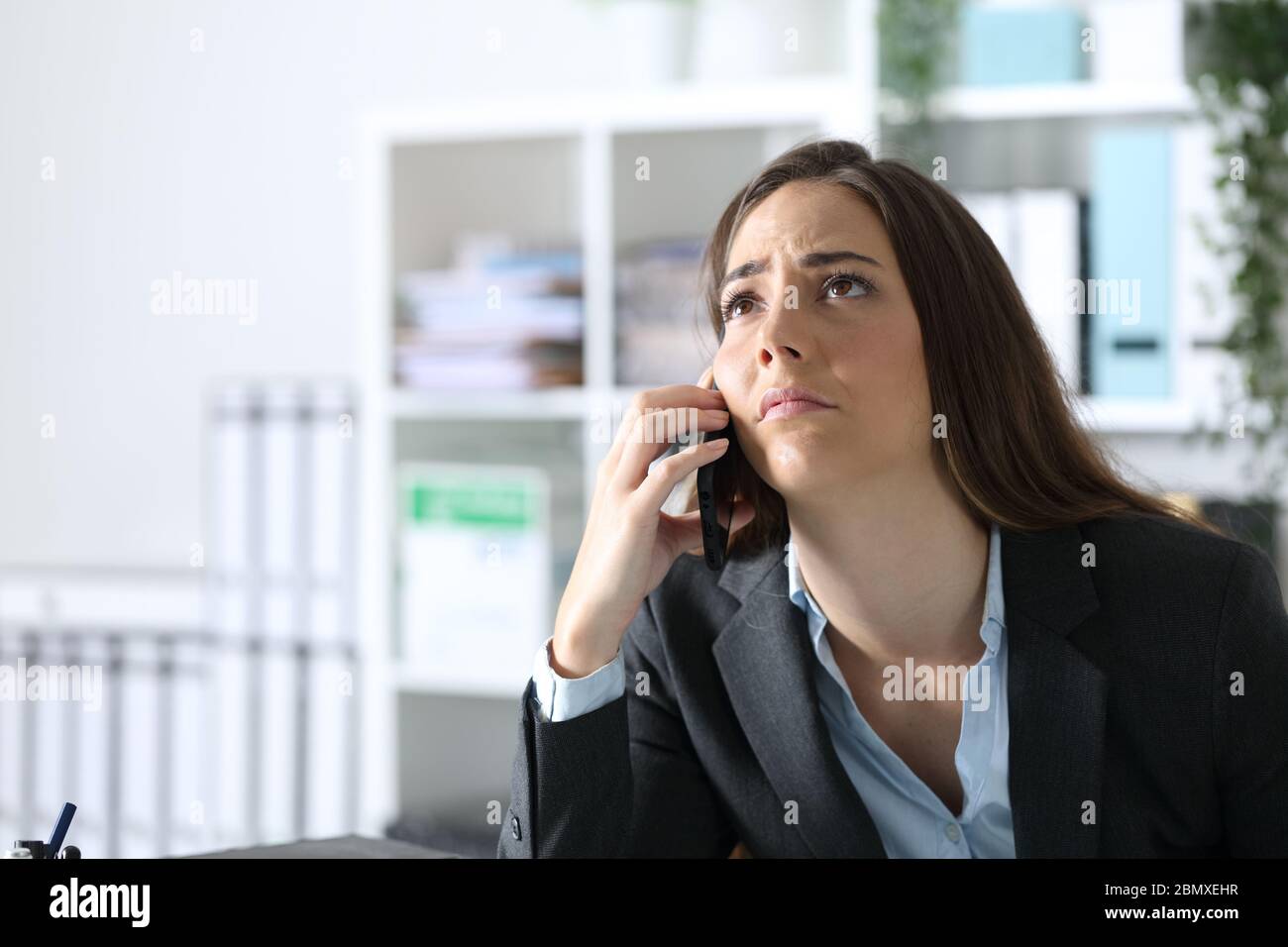 Femme dirigeante impatiente appelant sur un smartphone, regardant le bureau Banque D'Images