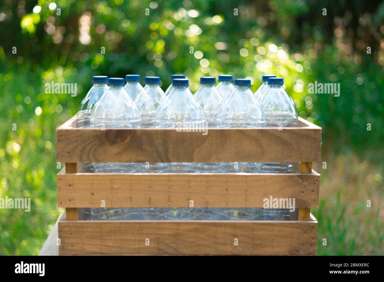 Réutilisation du concept de recyclage des bouteilles en plastique. Bouteilles en plastique avec bouchons dans une boîte en bois recyclé avec beau coucher de soleil dans le jardin Banque D'Images