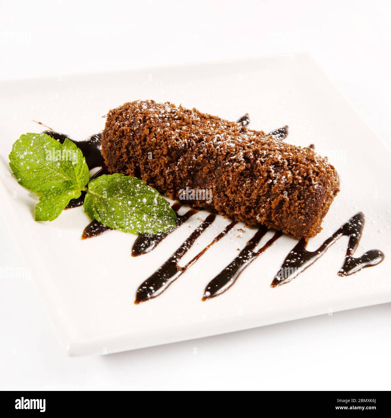 Un morceau de gâteau arrosé de sucre glace et décoré de menthe et de chocolat fondu sur une assiette carrée blanche Banque D'Images