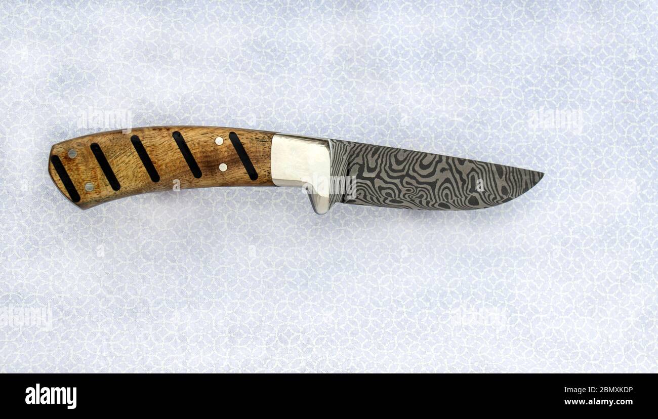 Un magnifique couteau à lame fixe de damas avec un motif zébré est exposé sur un tissu gris et blanc. La poignée unique est en bois de Myrtle. Bo Banque D'Images