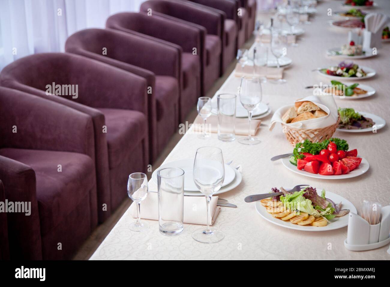 une table recouverte d'une nappe blanche avec des salades, des verres, des assiettes, des serviettes et un certain nombre de sièges Banque D'Images