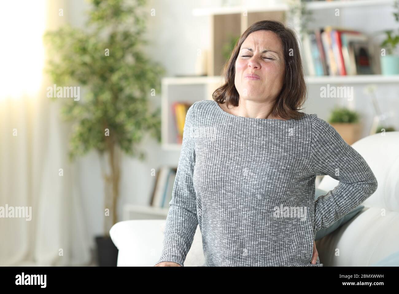 Femme adulte en douleur se plaignant de mal de dos assis sur un canapé à la maison Banque D'Images