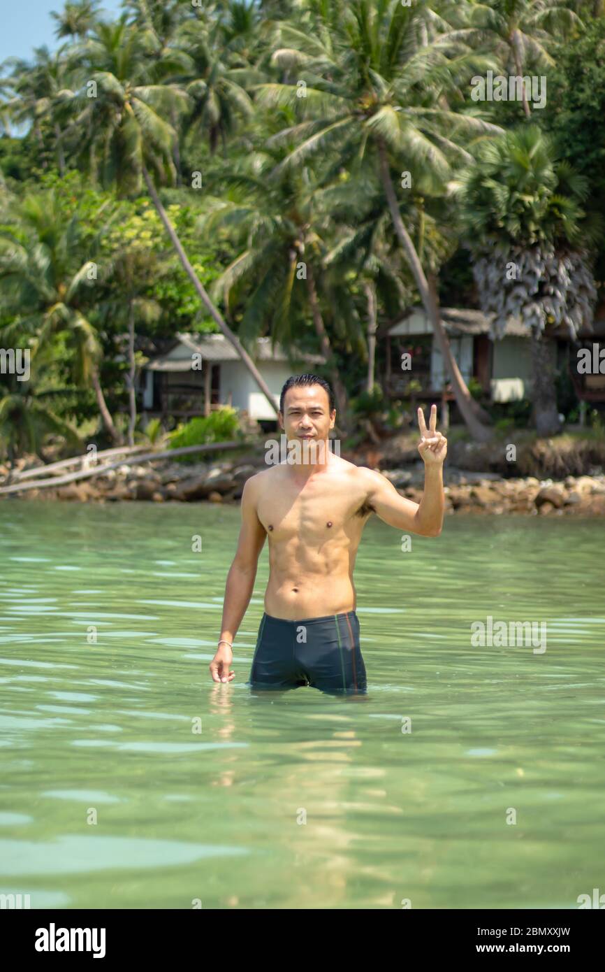 Les hommes asiatiques nager dans la mer des rochers et des arbres en arrière-plan. Banque D'Images