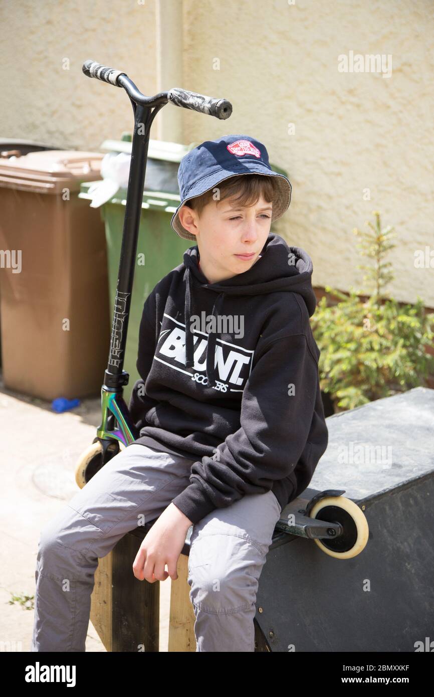 Un garçon de patineuse de 11 ans, avec un scooter de cascades assis sur une rampe. Banque D'Images