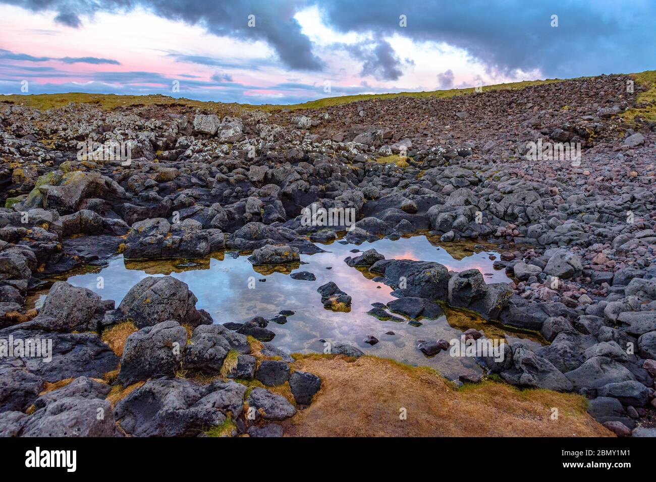 Nuages roses dynamiques se reflétant dans un bassin d'eau parmi les rochers d'un champ de lave à Arnarstapi, en Islande Banque D'Images