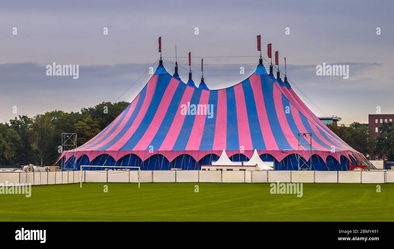 Tente de cirque avec rayures roses et bleues sur pelouse verte sous ciel d'été. Hébergement utilisé lors du festival d'été. Banque D'Images