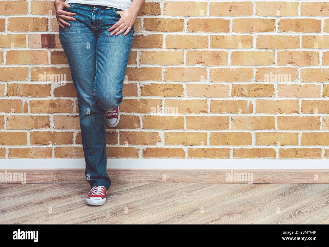 Femme jambes en jeans et rouge baskets, femme debout devant le mur de brique, mode concept Banque D'Images