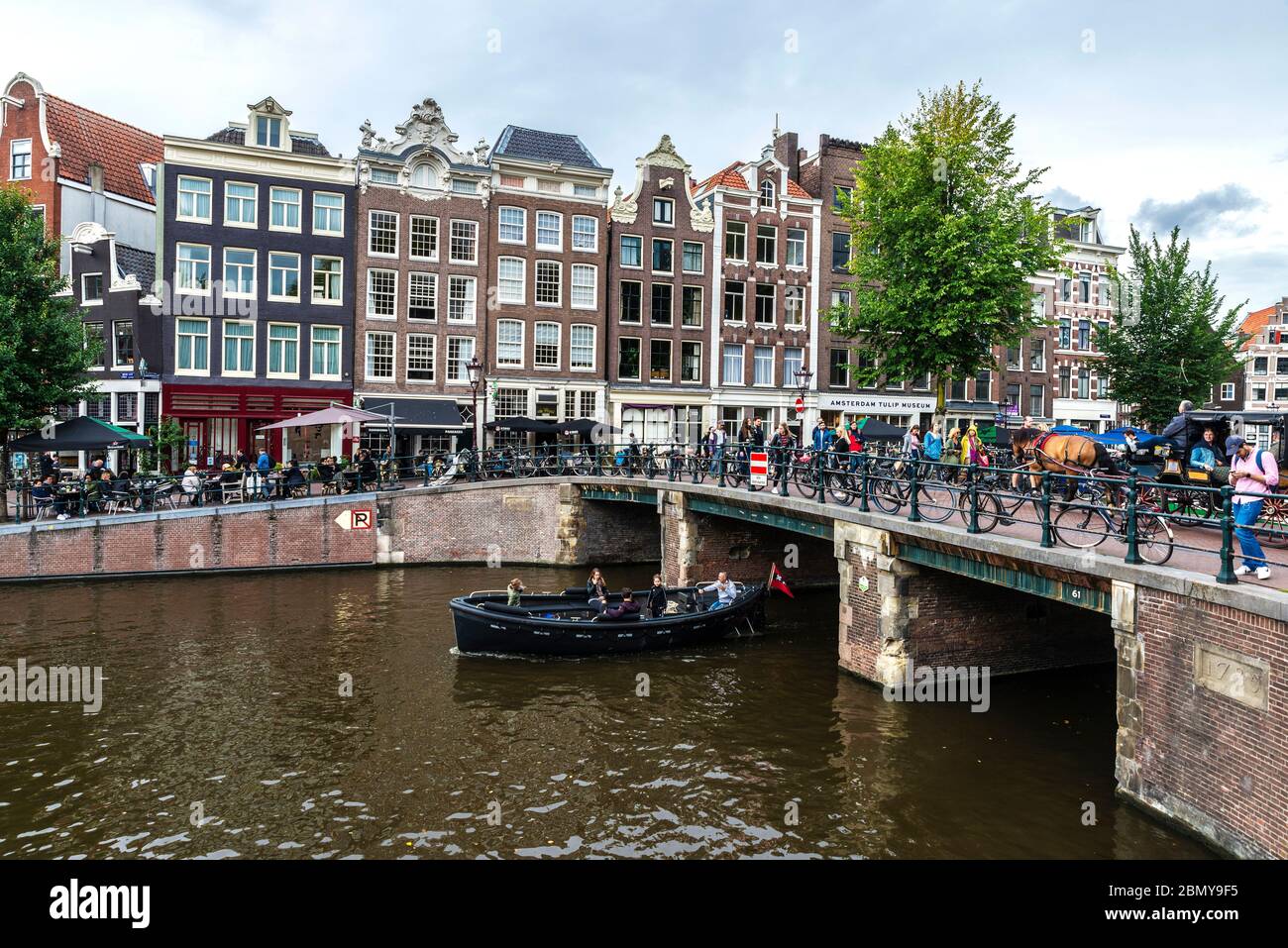 Amsterdam, pays-Bas - 8 septembre 2018 : vieilles maisons traditionnelles penchées le long d'un canal avec des gens sur les terrasses de bars et un bateau naviguant à Amsterdam Banque D'Images