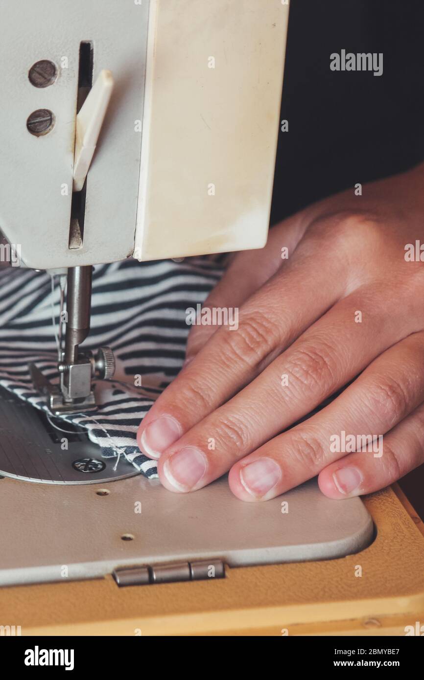 Femme mains utilisant la machine à coudre pour coudre le masque médical du visage pendant la pandémie du coronavirus. Masque de protection fait maison contre le virus. Masques de couture, COVID-19. Mise au point sélective partiellement floue. Banque D'Images