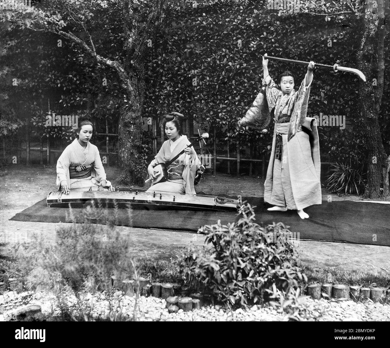 [ 1890 Japon - les femmes japonaises jouent de la musique ] — deux femmes jouent le shamisen et le koto tandis qu'une troisième danse avec une naginata, une arme de pôle traditionnellement utilisée par les membres de la classe samouraï. D'une série de diapositives en verre publiées (mais non photographiées) par le photographe écossais George Washington Wilson (1823–1893). La société Wilson était l’un des plus grands éditeurs de tirages photographiques au monde. diapositive en verre vintage du xixe siècle. Banque D'Images