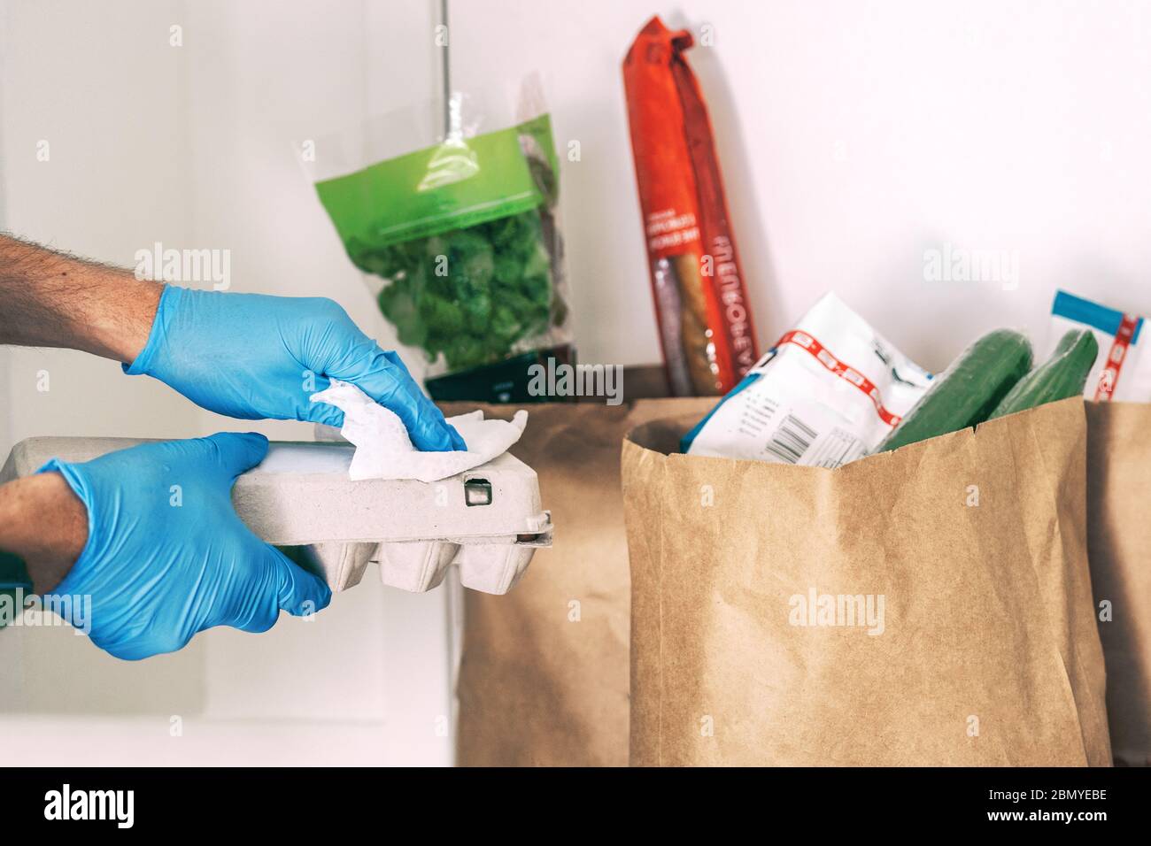 COVID-19 - est-il nécessaire de nettoyer vos provisions livrées à la maison. Un homme en quarantaine essuyant l'emballage en carton avec des lingettes désinfectantes après le magasinage Banque D'Images
