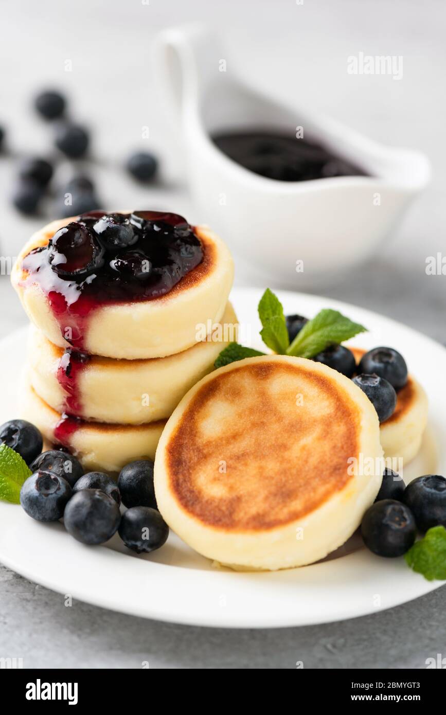 Beignets de fromage Syrniki avec confiture de myrtilles sur une assiette blanche. Cuisine russe ukrainienne saine nourriture pour le petit déjeuner Banque D'Images