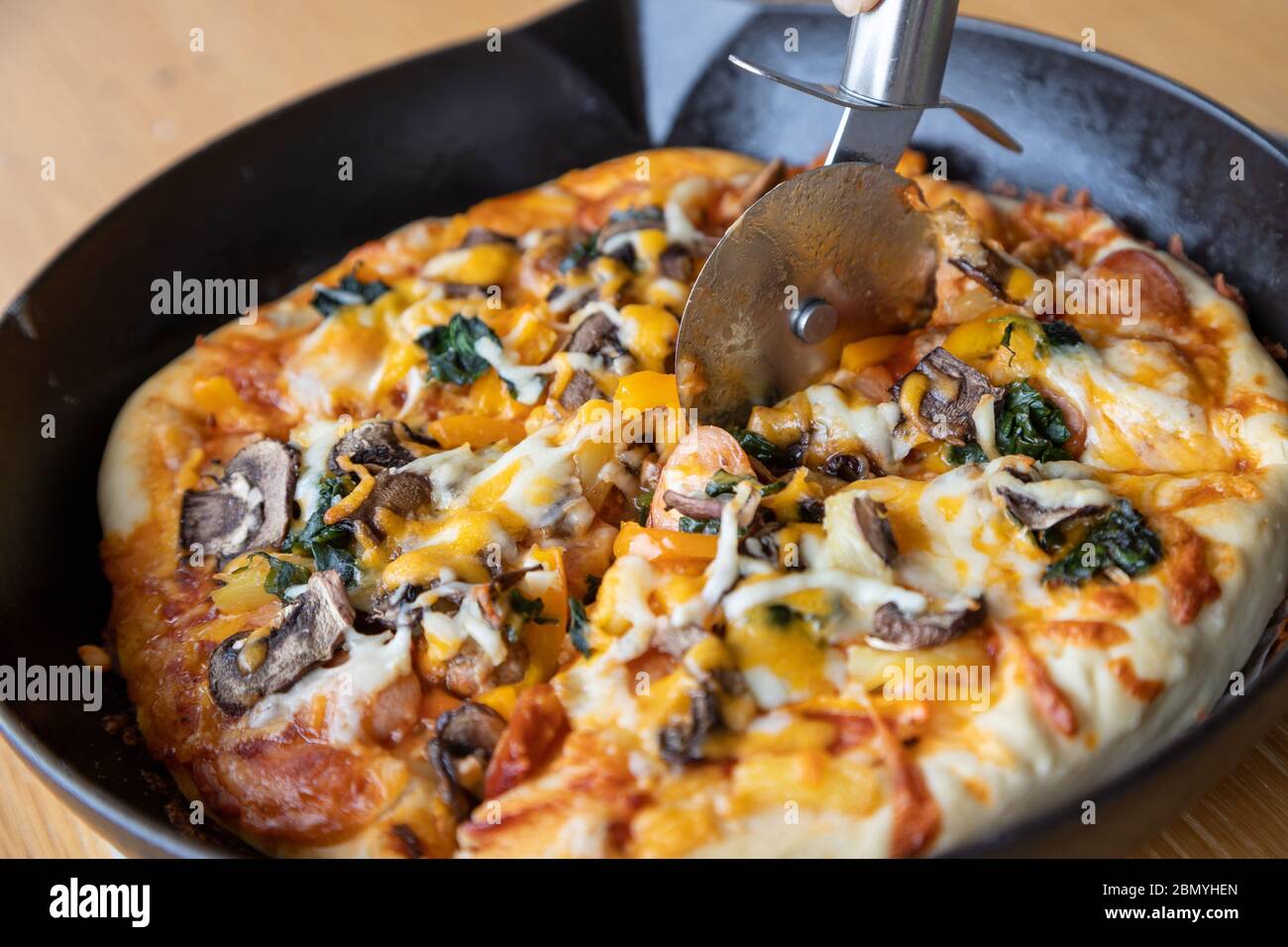 Coupe-pizza trancheuse de pizza végétarienne maison avec champignons, épinards, oignon, fromage, poivron et variété de garnitures de légumes et de h aromatique Banque D'Images