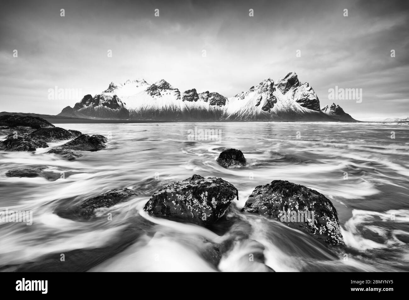 Image en noir et blanc d'une formation de montagne enneigée reflétée dans l'eau d'une plage de sable noir de lave, dans les vagues de premier plan lavées autour de b Banque D'Images