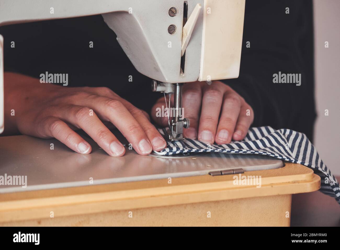 Les mains des femmes utilisant la machine à coudre pour coudre un masque médical coloré du visage pendant la pandémie de coronavirus. Masque de protection fait maison contre le virus. Masques à coudre, COVID-19. Mise au point sélective. Banque D'Images