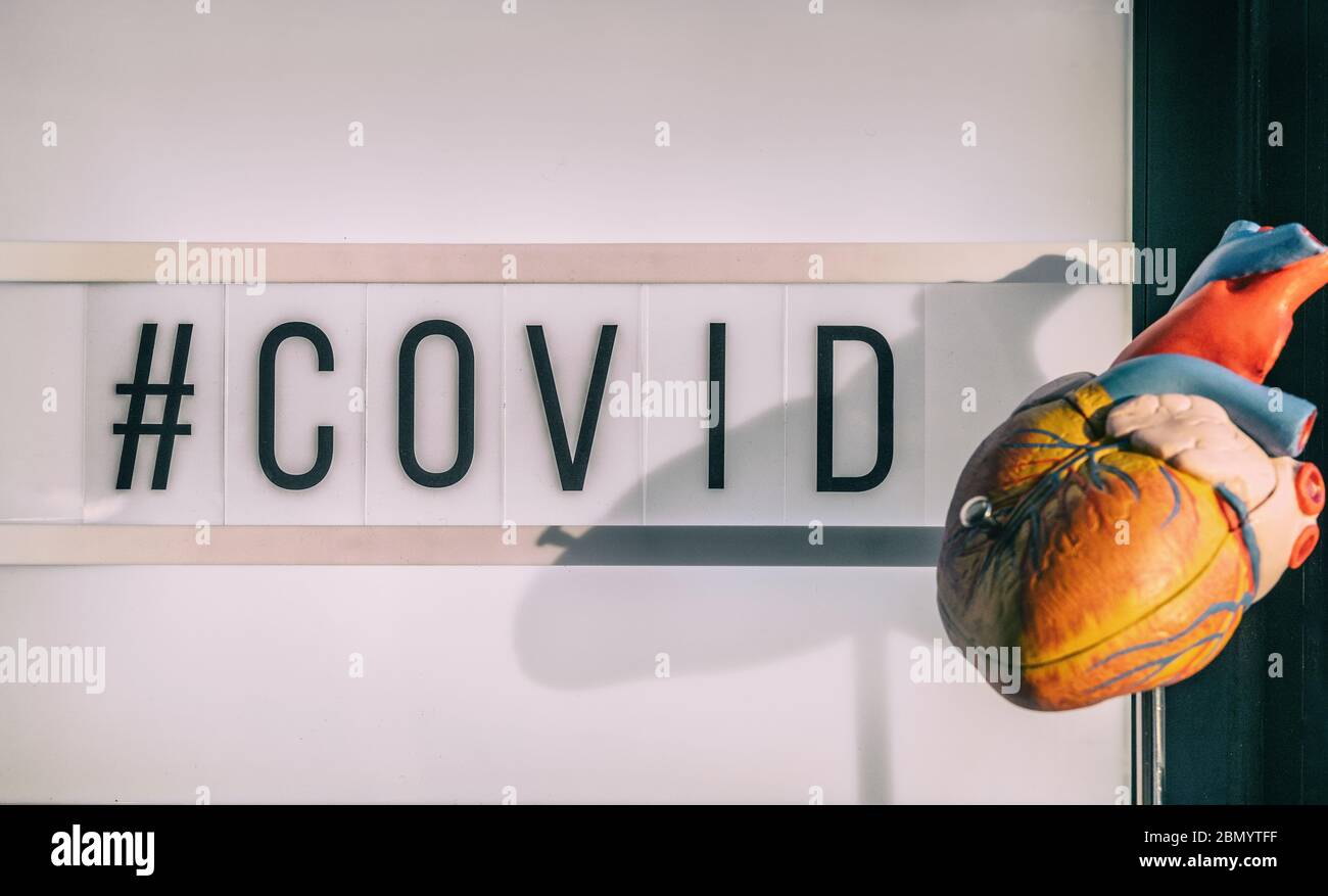 Le signe de hashtag COVID-19 à côté du modèle cardiaque médical montrant le risque cardiovasculaire d'accident vasculaire cérébral caillot de sang avec infection à coronavirus. Texte du panneau d'affichage de la visionneuse Banque D'Images