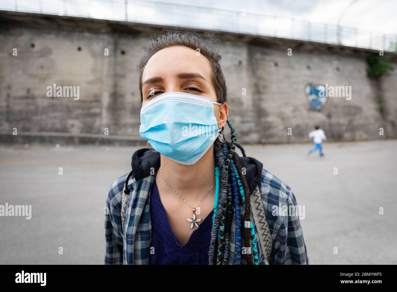 portrait d'une jeune femme rebelle avec une coiffure rasta dans un cadre urbain portant un masque de protection couvrant son visage et laissant voir ses yeux fac Banque D'Images