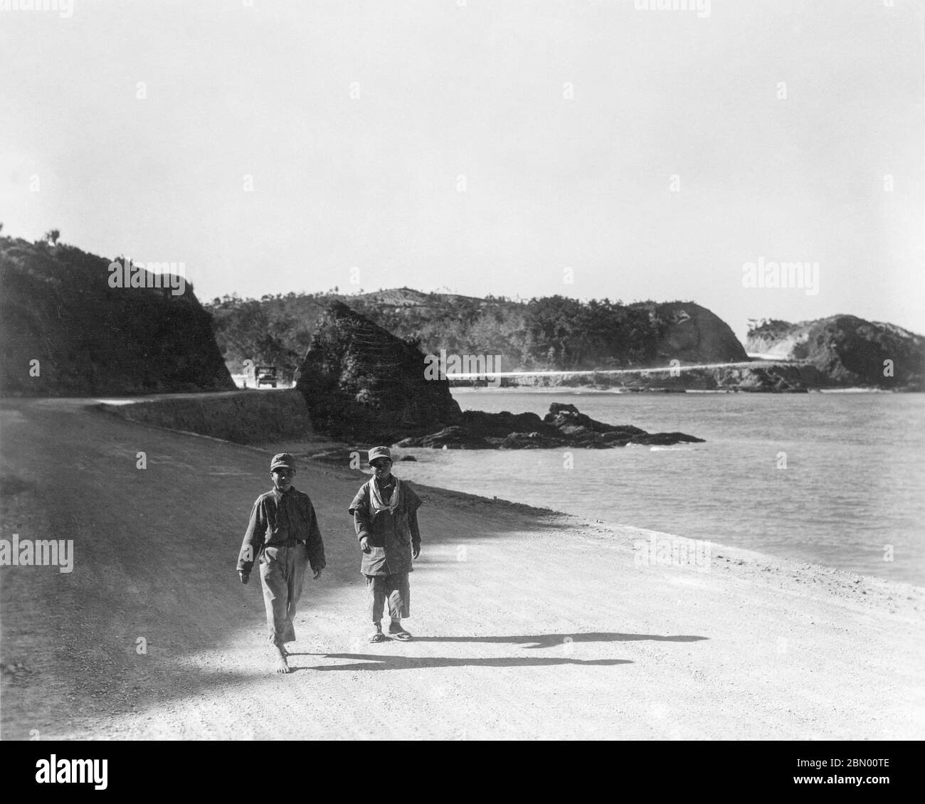 1946 Japon - garçons d'Okinawa ] — deux garçons d'Okinawa portant des  vêtements militaires excédentaires marchant sur la route I pendant  l'occupation américaine précoce d'Okinawa, 1946 (Showa 21). Dans le dos,