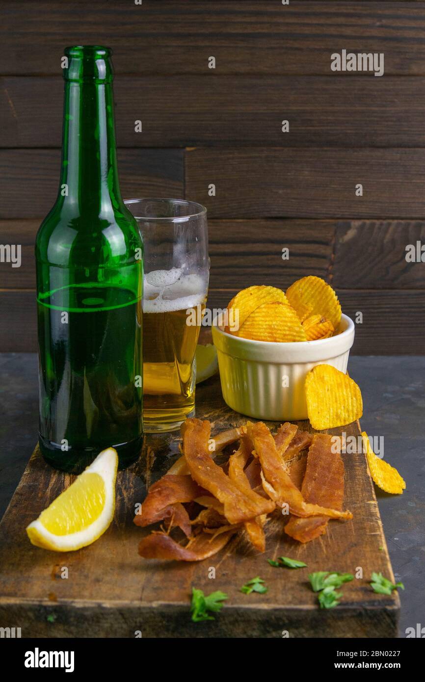 Calmar péruvien avec bière, citron et chips de pomme de terre sur un panneau en bois sombre. En-cas sur le poisson avec de la bière. Gros plan Banque D'Images