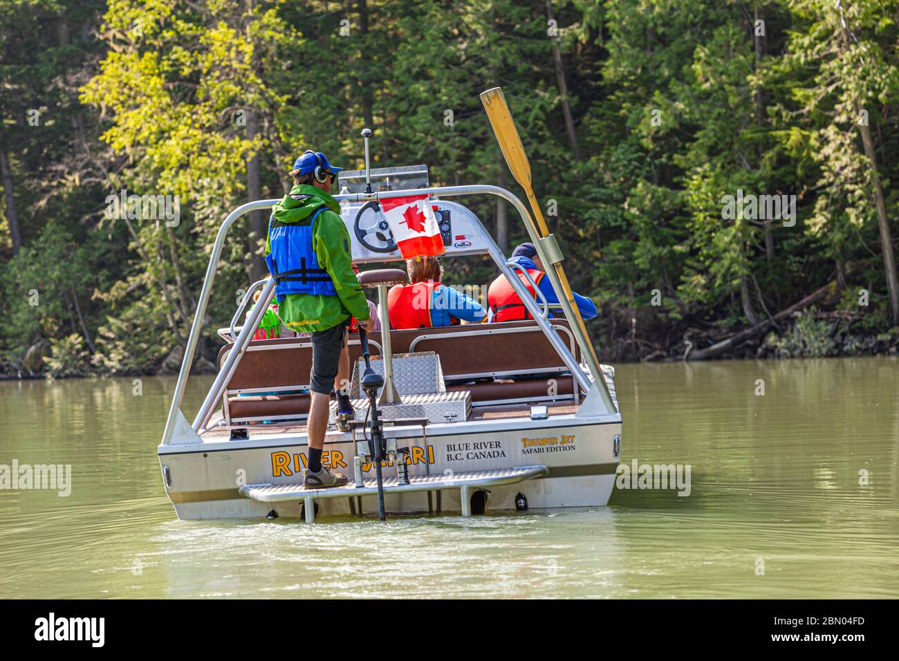Vue arrière du bateau à réaction « River Safari » de Blue River : le guide se tient à la barre, les passagers en gilets de sauvetage rouges sont assis devant lui, un drapeau canadien flotte à la proue. District régional de Thompson-Nicola, Colombie-Britannique, Canada Banque D'Images