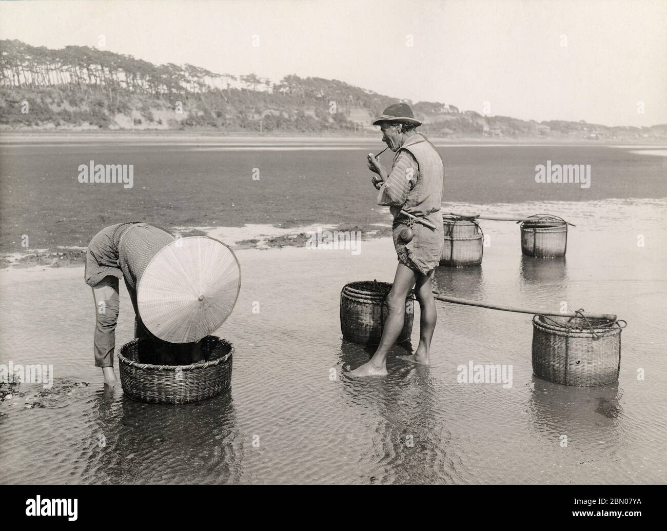 [ Japon des années 1920 - chasseurs de crevettes japonais ] — deux hommes pêchant des crevettes sur la plage de la baie de Tokyo. On fume un tuyau. imprimé gélatine argent du xxe siècle. Banque D'Images