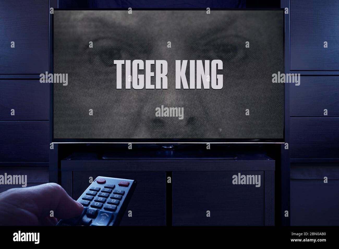 Un homme pointe une télécommande vers le téléviseur qui affiche l'écran principal du titre Tiger King (usage éditorial uniquement). Banque D'Images