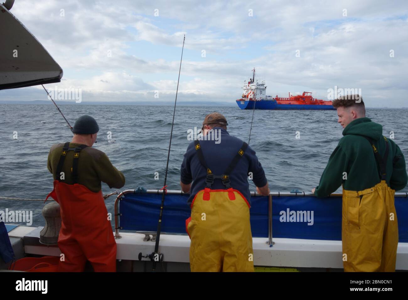 Trois messieurs, pêche de plaisir sur un bateau de pêche en mer du Nord en dehors de Hartlepool, un bateau-citerne à gaz passe en arrière-plan. Banque D'Images