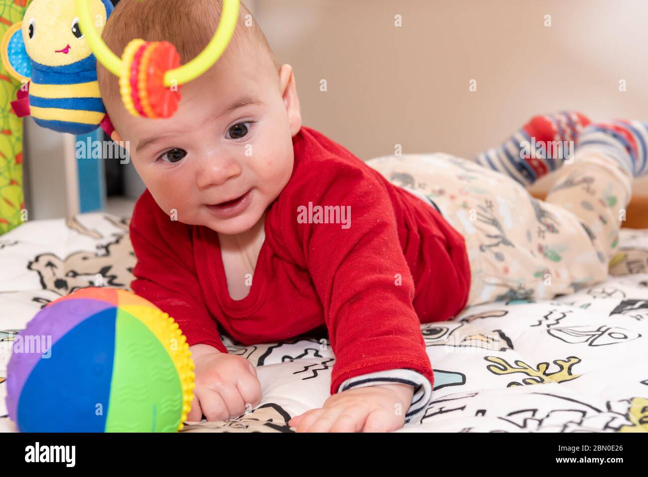 Un petit garçon mignon pendant le ventre, regardant l'appareil photo. enfant de 6 mois avec expression de curiosité sur son visage entouré de jouets colorés. Banque D'Images