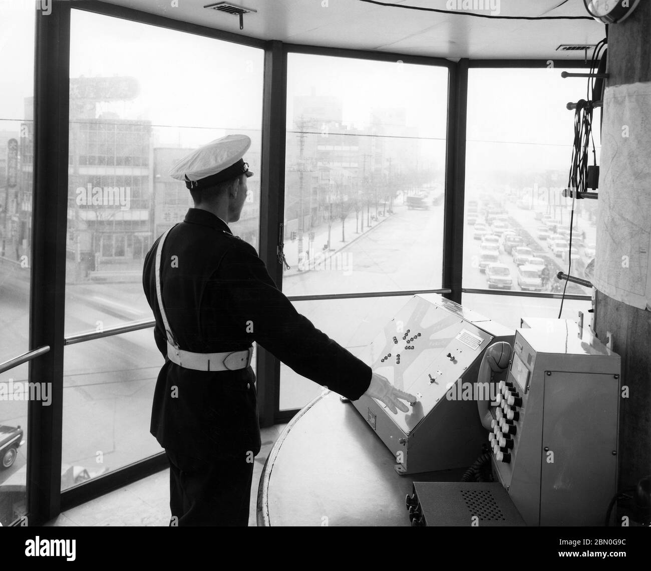 [ années 1960 Japon - Tour de contrôle de la circulation d'Ikebukuro, Tokyo ] — UN policier japonais observe la circulation depuis la Tour de contrôle de la circulation (コントロールタワー・操車室) au Rotary de Mutsumata (六ツ又交差点) à Ikebukuro, Tokyo, ca. 1965 (Showa 40). La tour de 11 mètres de haut a commencé ses opérations en novembre 1962 (Showa 37) et a réduit les accidents qui se sont produits à cet endroit de plusieurs centaines à quelques dizaines. La tour a été démoli le 22 août 1968 (Showa 43) pour permettre la construction de l'autoroute surélevée route 5. imprimé gélatine argent du xxe siècle. Banque D'Images