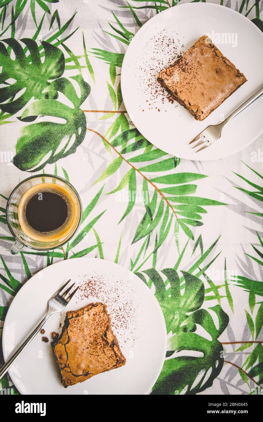 Vue de dessus d'une tasse de café et de deux assiettes à dessert avec gâteau au brownie sur une nappe à motif feuilles vertes. Banque D'Images
