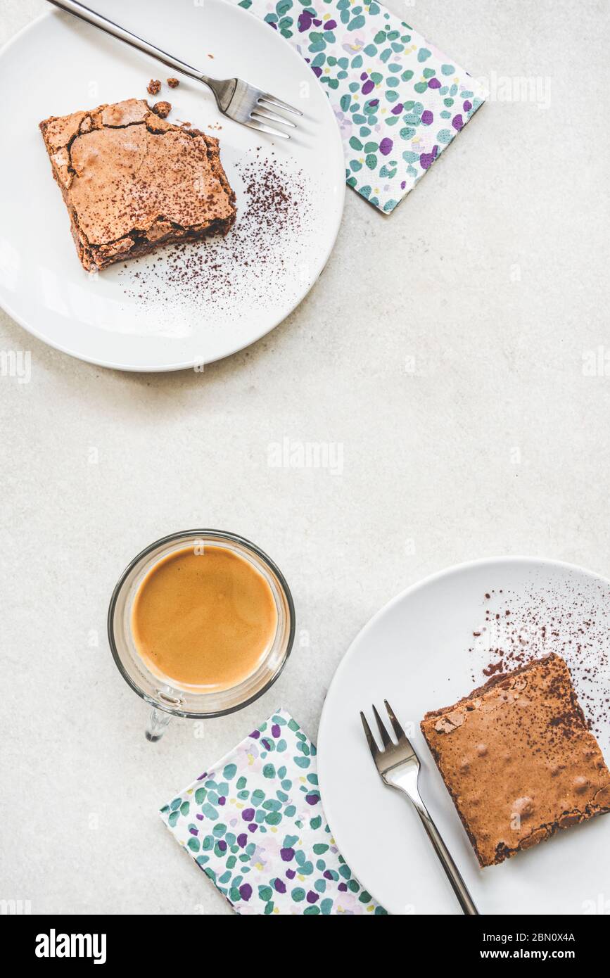 Vue de dessus d'une tasse de café et de deux assiettes à dessert avec gâteau au brownie sur fond rustique blanc. Banque D'Images