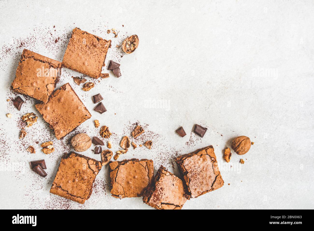 Vue de dessus du gâteau maison au brownie fraîchement préparé avec des noix, du chocolat et de la poudre de cacao sur fond rustique blanc. Banque D'Images