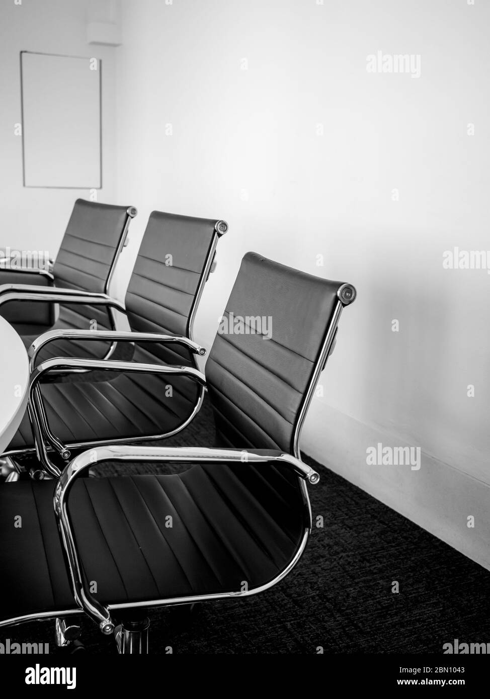 Décoration moderne de la salle de conférence, trois chaises en cuir de luxe noir près de la table et un mur blanc vide. Salle de réunion blanche dans le bureau, style vertical Banque D'Images