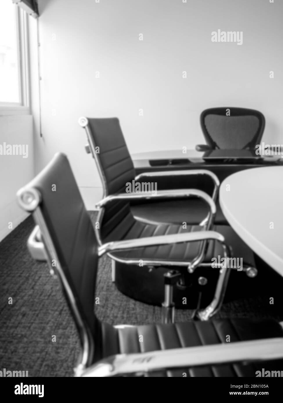 Décor flou et moderne de la salle de conférence, trois chaises en cuir noir de luxe près de la table. Salle de réunion blanche au bureau, verticale Banque D'Images