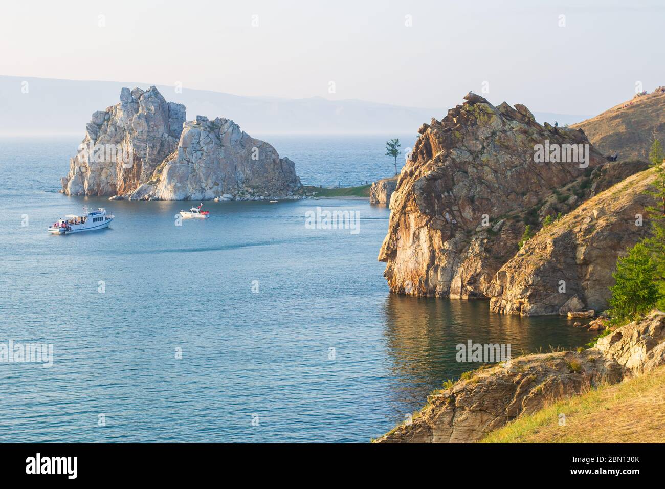 La côte rocheuse de l'île d'Olkhon et du Cap Burhan, en soirée d'été, aux rayons du soleil couchant. Bateaux de plaisance dans les eaux bleues du lac Baikal Banque D'Images