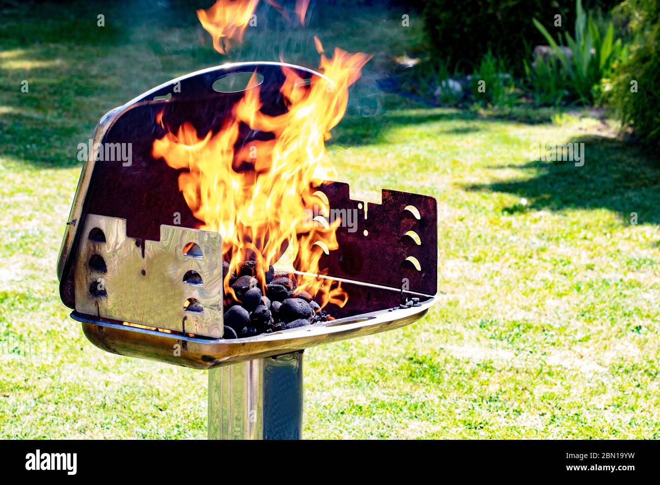 Gros plan du moment gelé des flammes flamboyantes dans un grill au charbon de bois avec fond d'herbe verte d'un jardin. Prépearing d'une fête barbecue à a s. Banque D'Images