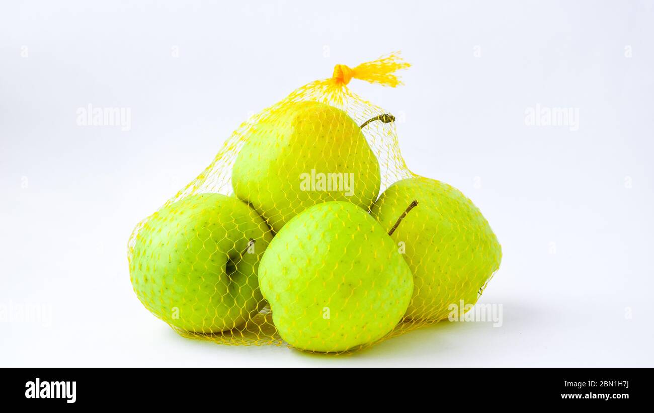 Un groupe de pommes dans un filet orange accroché devant un mur blanc. Tendance. Le concept de régime alimentaire et de saine alimentation verte Granny Smith et or Banque D'Images