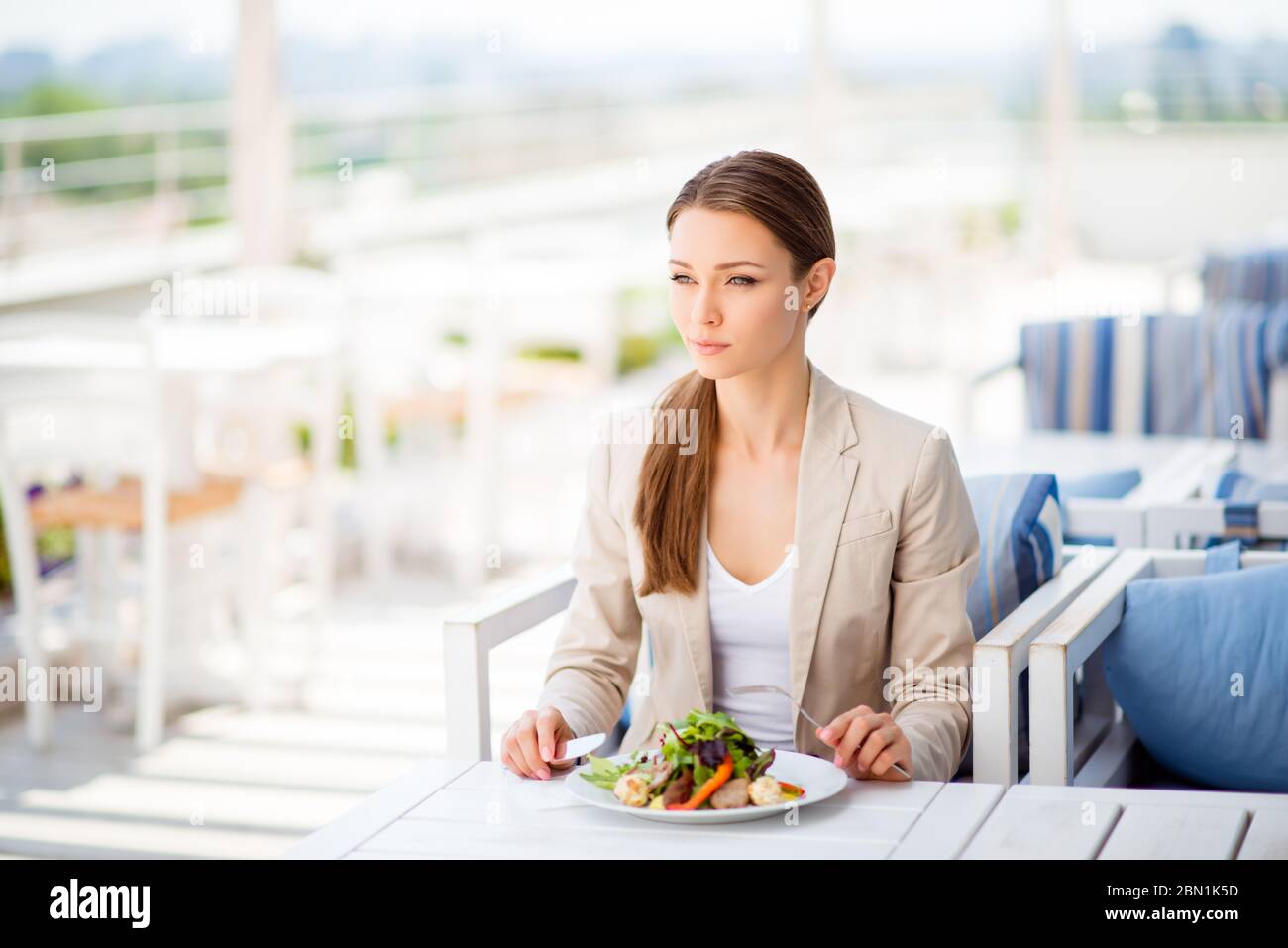 Une jeune femme d'affaires pensive prend son déjeuner sur la terrasse lumineuse en plein air du restaurant sur le toit, elle est dans des vêtements formels et avec une queue de poney Banque D'Images